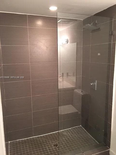 Walk-in shower featuring large-format horizontal wall tiles, a frameless glass enclosure, a square rainfall shower head, and a mosaic tile floor