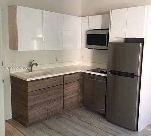 Kitchen featuring high-gloss white upper cabinetry, wood-finish lower cabinetry, white solid-surface countertops, integrated stainless steel appliances, and wood-finish flooring