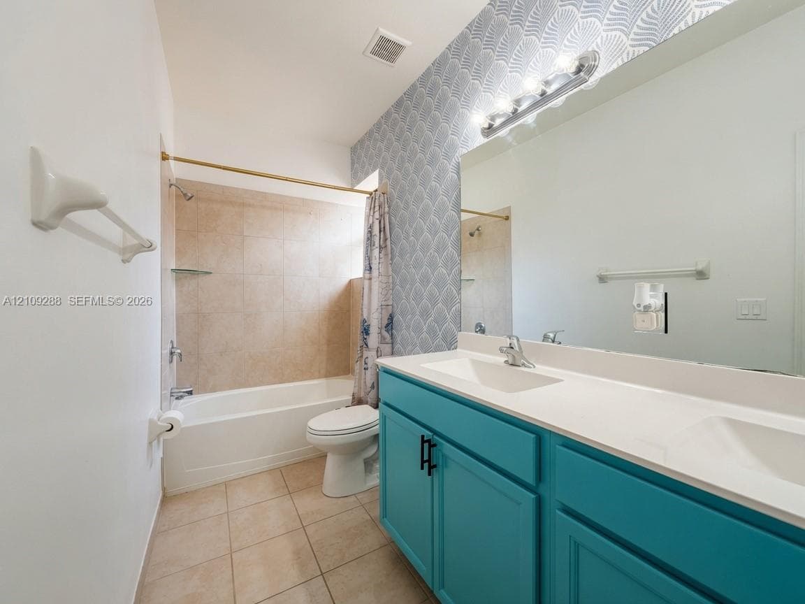 Dual-sink vanity with matte black hardware and white countertop, patterned wall covering, and a tub-shower combination with tiled surround