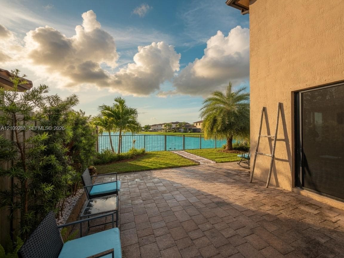 Paver patio featuring a manicured lawn, metal perimeter fencing, and water frontage