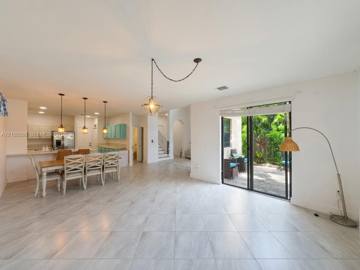 Open-concept interior featuring large-format tile flooring, recessed lighting, triple pendant fixtures, and sliding glass doors to a stone-paved patio