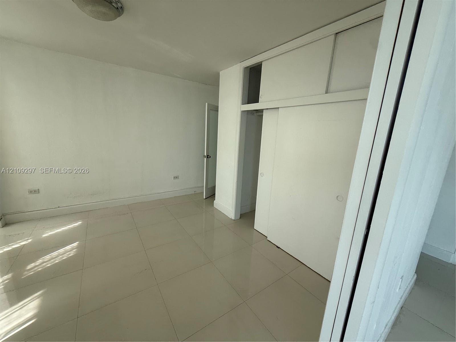 Room featuring large-format tile flooring, ceiling-mounted lighting, and built-in floor-to-ceiling closet cabinetry with sliding doors