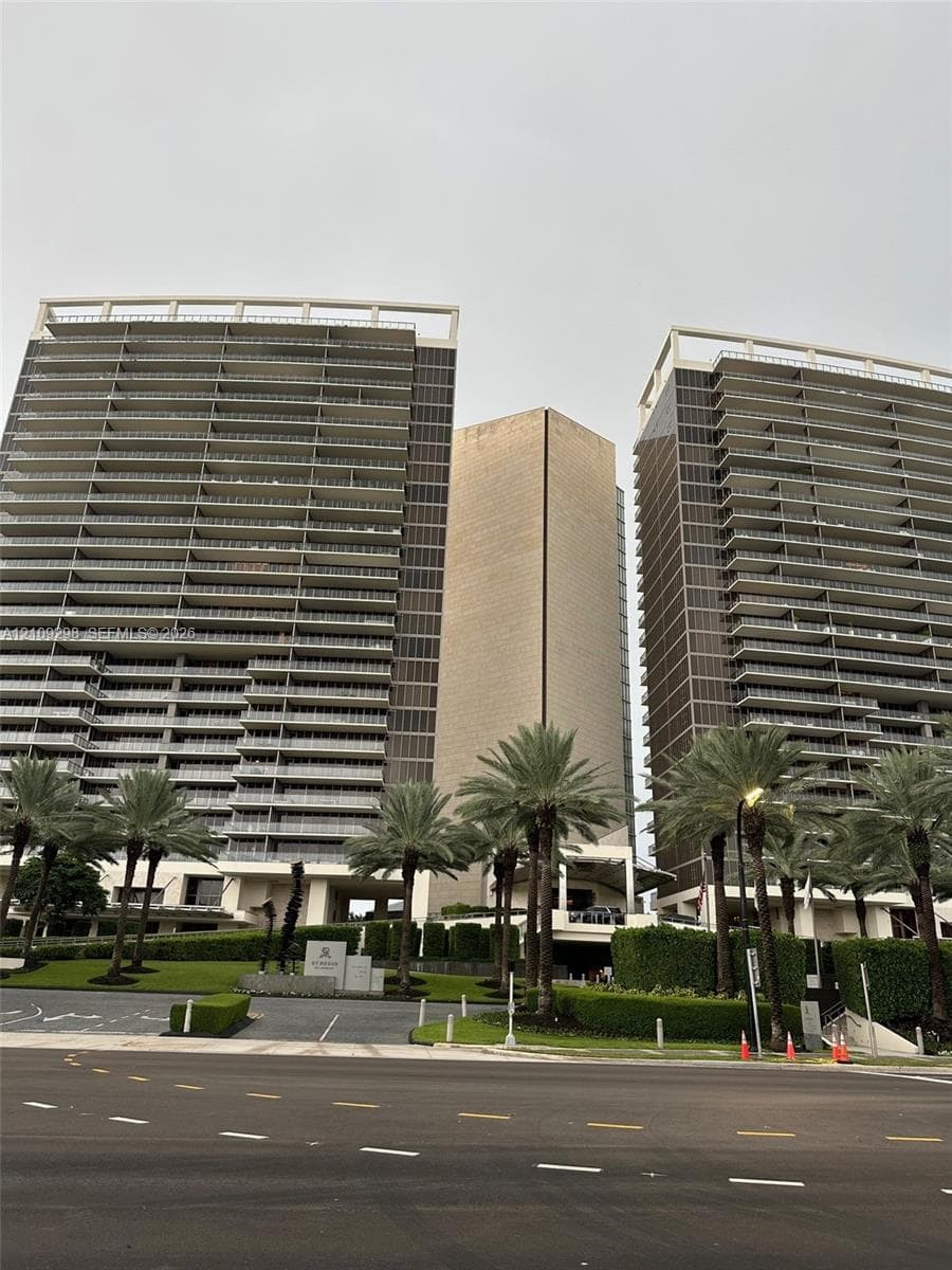Expansive interior featuring parquet wood flooring, floor-to-ceiling curved glass wall panels, recessed lighting, and a metal-railed balcony with ocean scenery