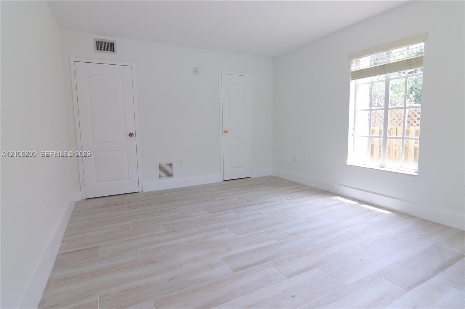 Neutral interior space featuring wood-finish tile flooring, multi-pane window with blinds, and two solid-core interior doors