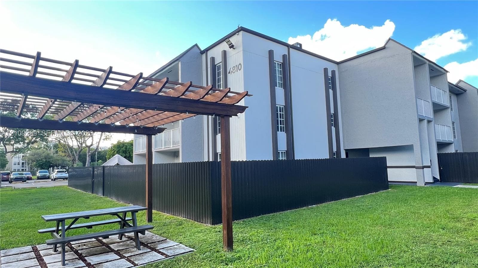 Exterior featuring a multi-story structure with a contemporary facade, wood-frame pergola, metal perimeter fencing, and landscaped grounds
