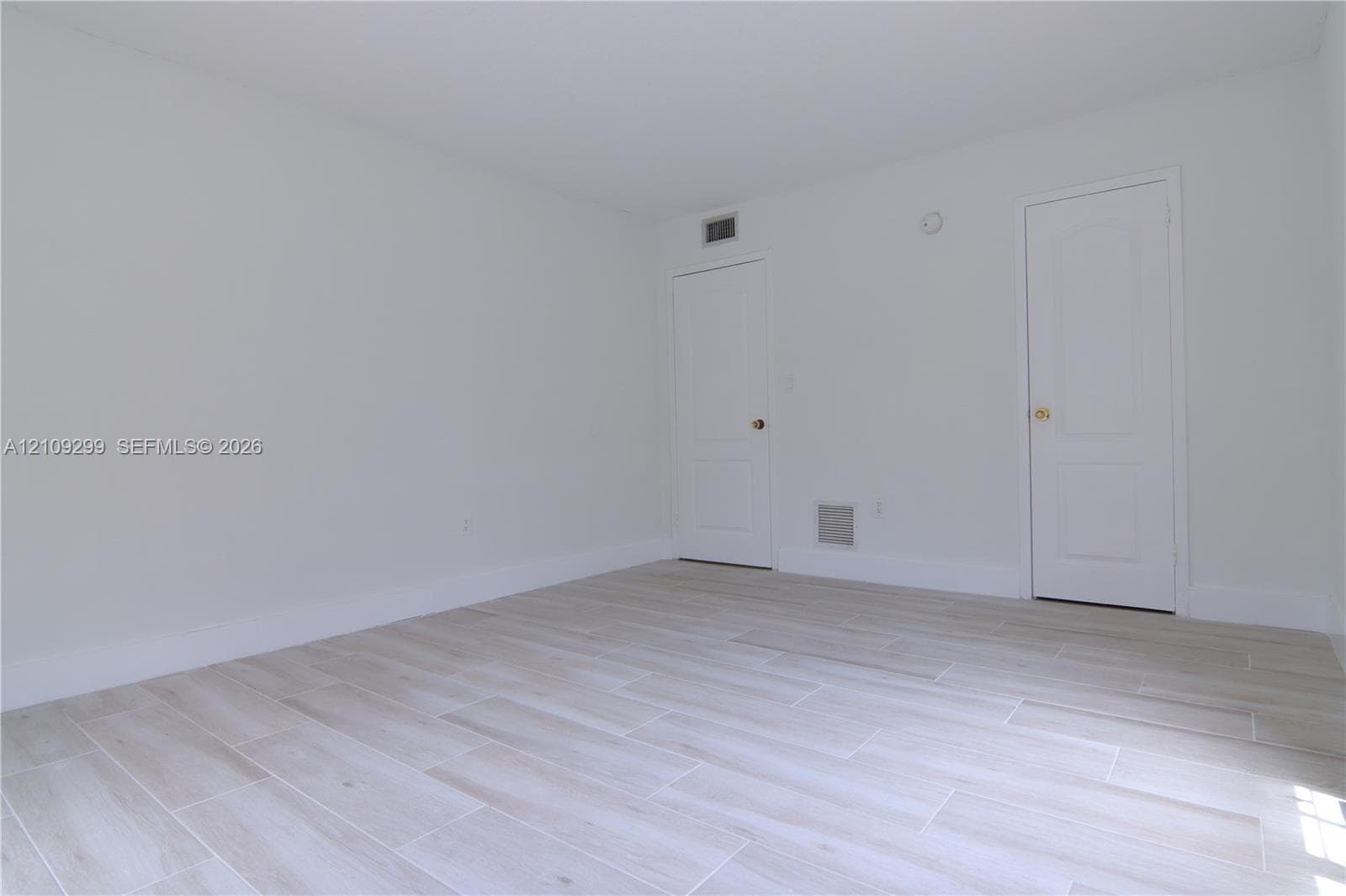 Neutral interior featuring wood-finish flooring, white walls, and two raised-panel doors with metallic hardware