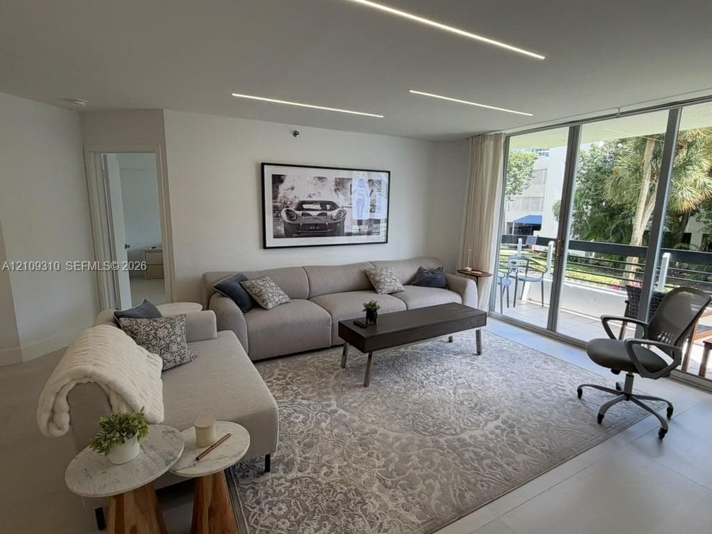 Living area featuring floor-to-ceiling glass sliding doors, neutral tile flooring, and integrated linear recessed ceiling lighting