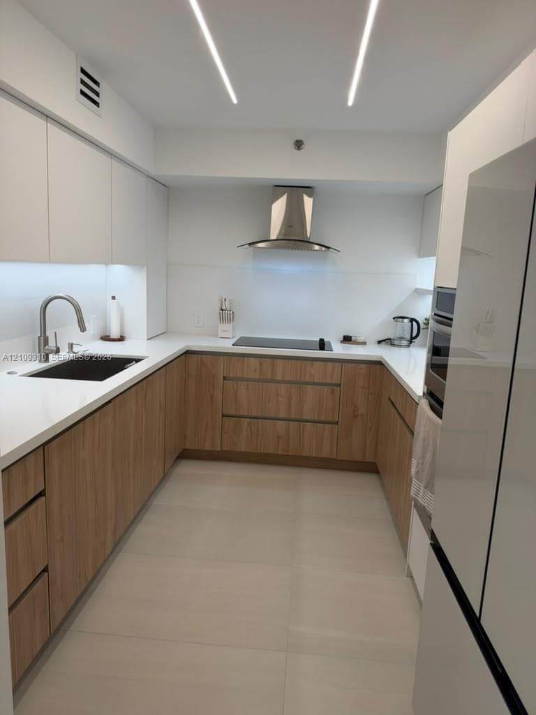 Modern kitchen featuring wood-finish cabinetry, solid-surface countertops, undermount sink with gooseneck faucet, stainless steel range hood, and linear recessed lighting