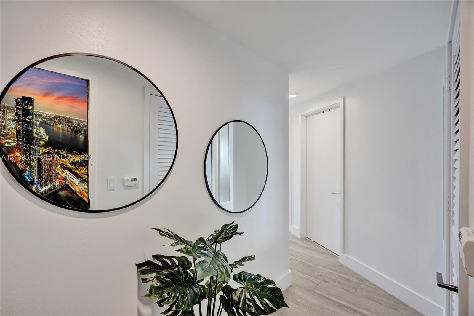 Hallway featuring wood-finish flooring, two circular wall-mounted mirrors with thin black frames, and louvered-style closet doors