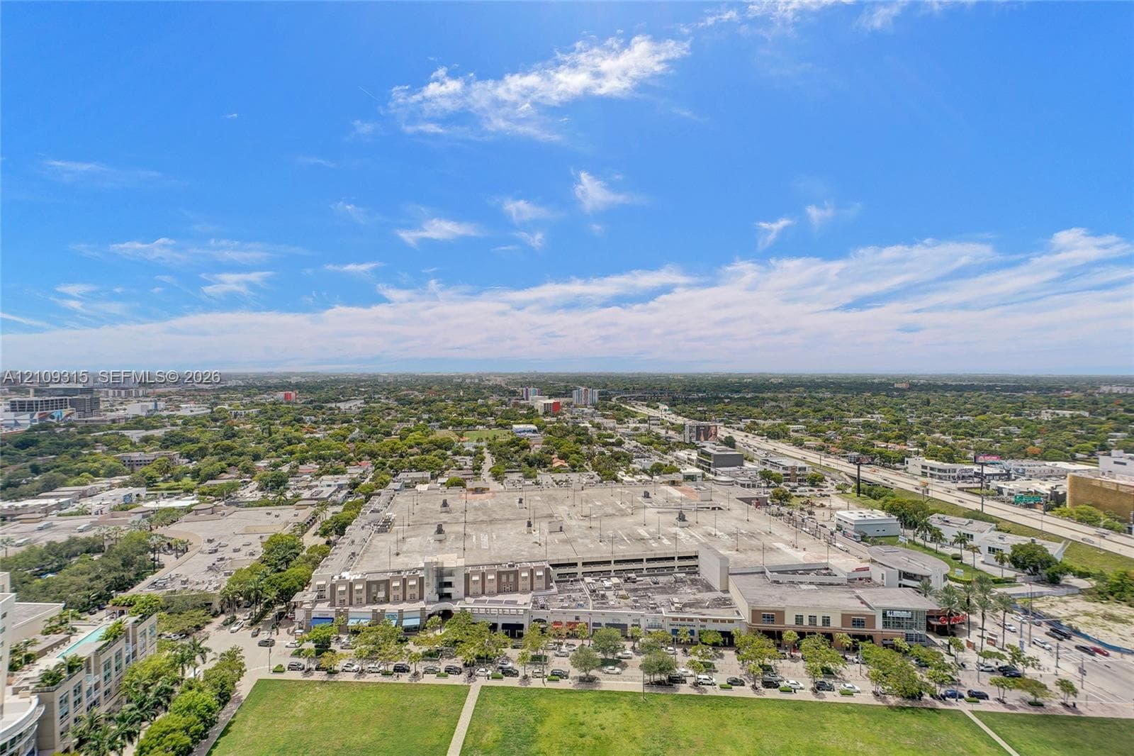 Aerial perspective of the urban landscape featuring expansive green space and proximity to a commercial complex