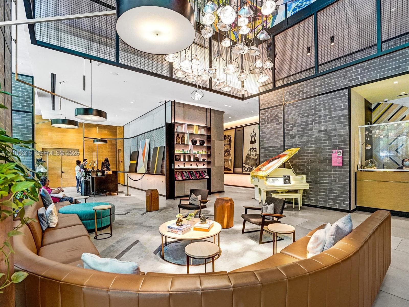 Expansive lobby featuring textured gray brick walls, multi-tiered sculptural light fixtures, floor-to-ceiling metal-framed glass partitions, and built-in recessed shelving