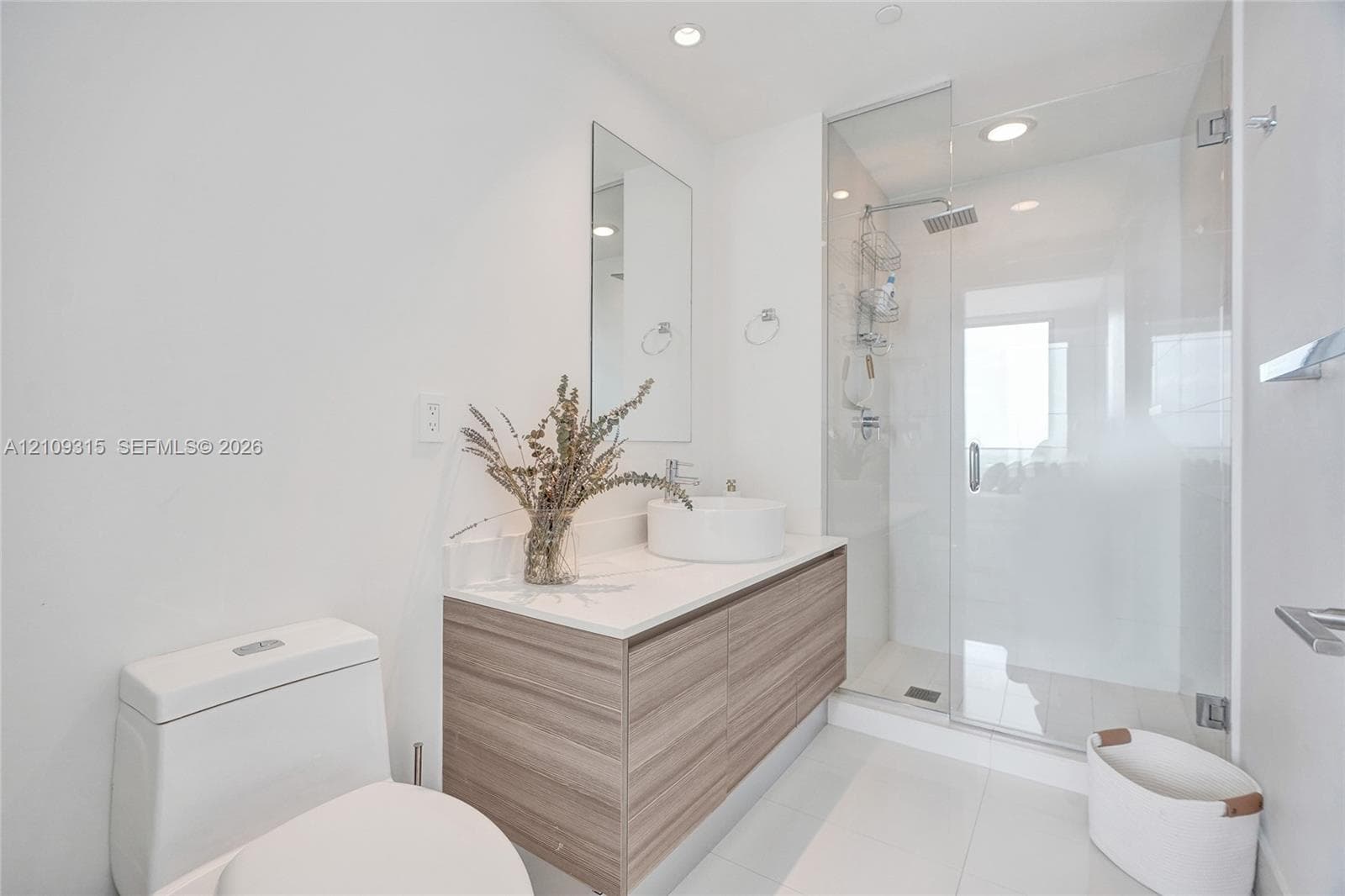 Floating wood-finish vanity with a white countertop and circular vessel sink, paired with a glass-enclosed walk-in shower featuring a rainfall showerhead
