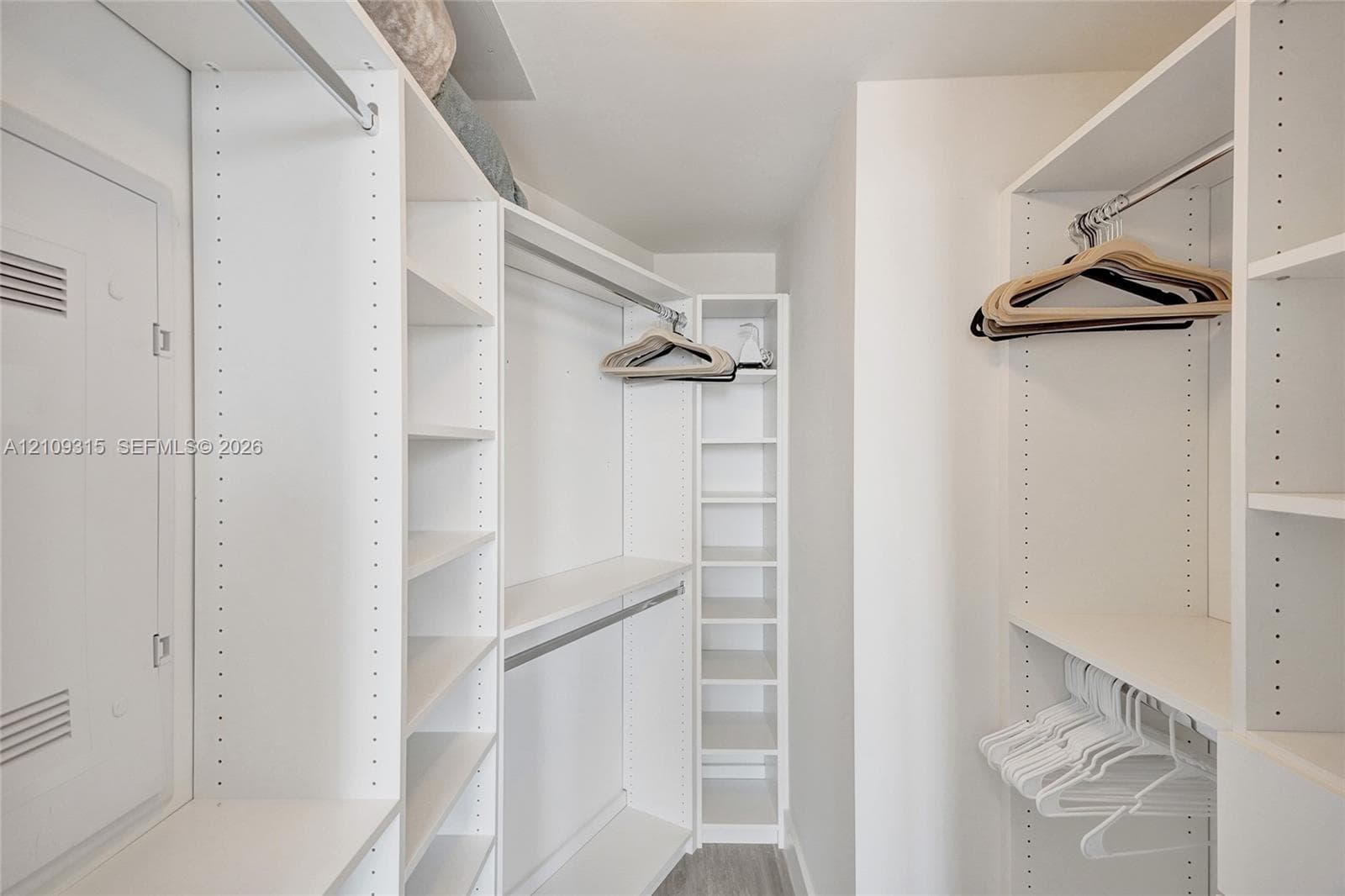 Walk-in closet featuring white custom built-in shelving, adjustable storage racks, and multiple tiered hanging rods