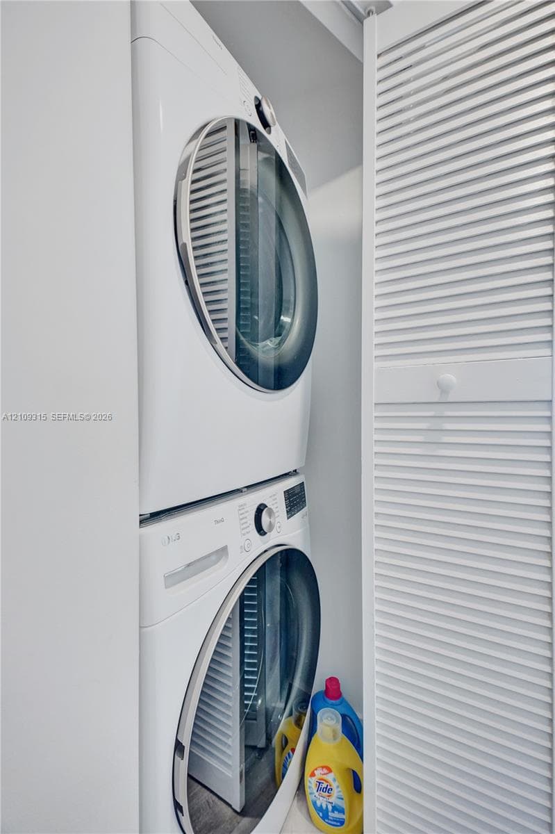 Stacked front-loading washer and dryer set enclosed by white louvered bi-fold doors