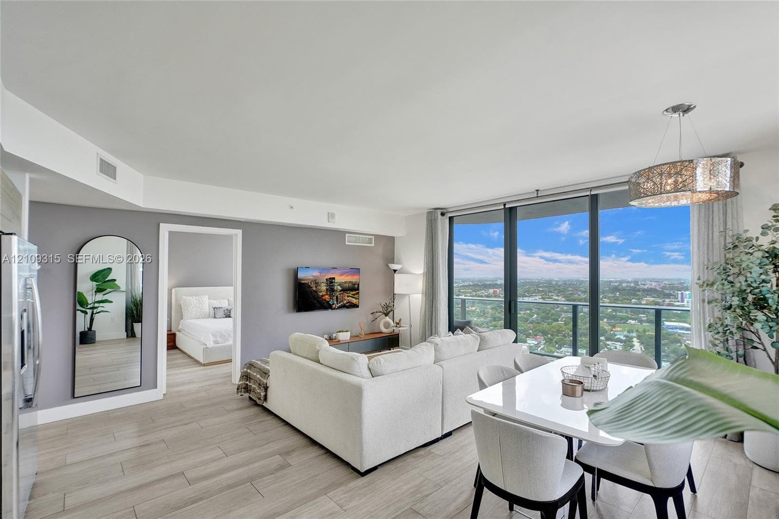 Open-concept living space featuring floor-to-ceiling windows, wood-finish flooring, a drum pendant light fixture, and an expansive balcony