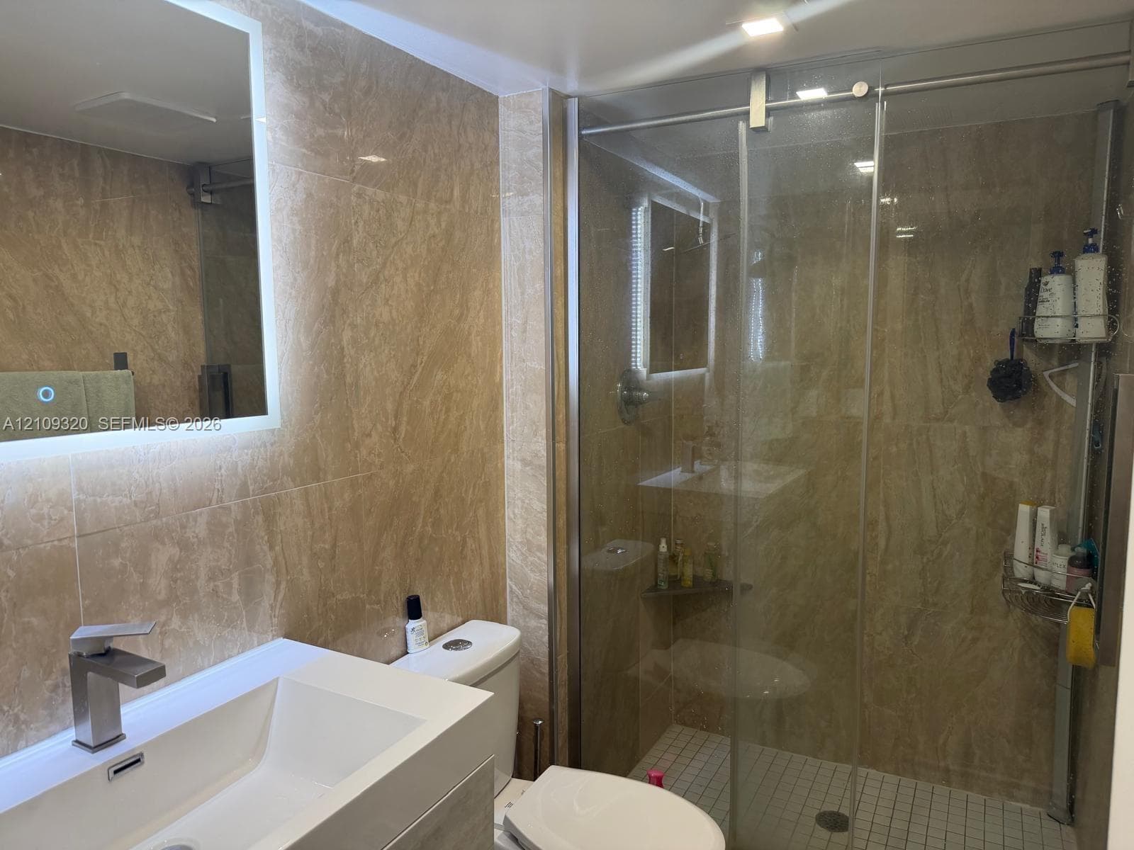 Bathroom featuring full-height stone-finish wall tiling, a glass-enclosed shower with a mosaic-tile floor, and a modern vanity with a rectangular basin and integrated LED-backlit mirror