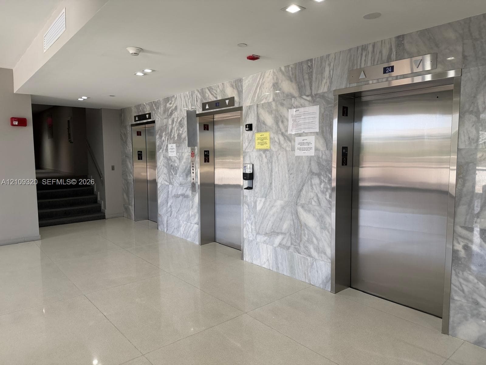 Elevator lobby featuring stone-clad wall accents, stainless steel elevator doors, recessed lighting, and polished flooring