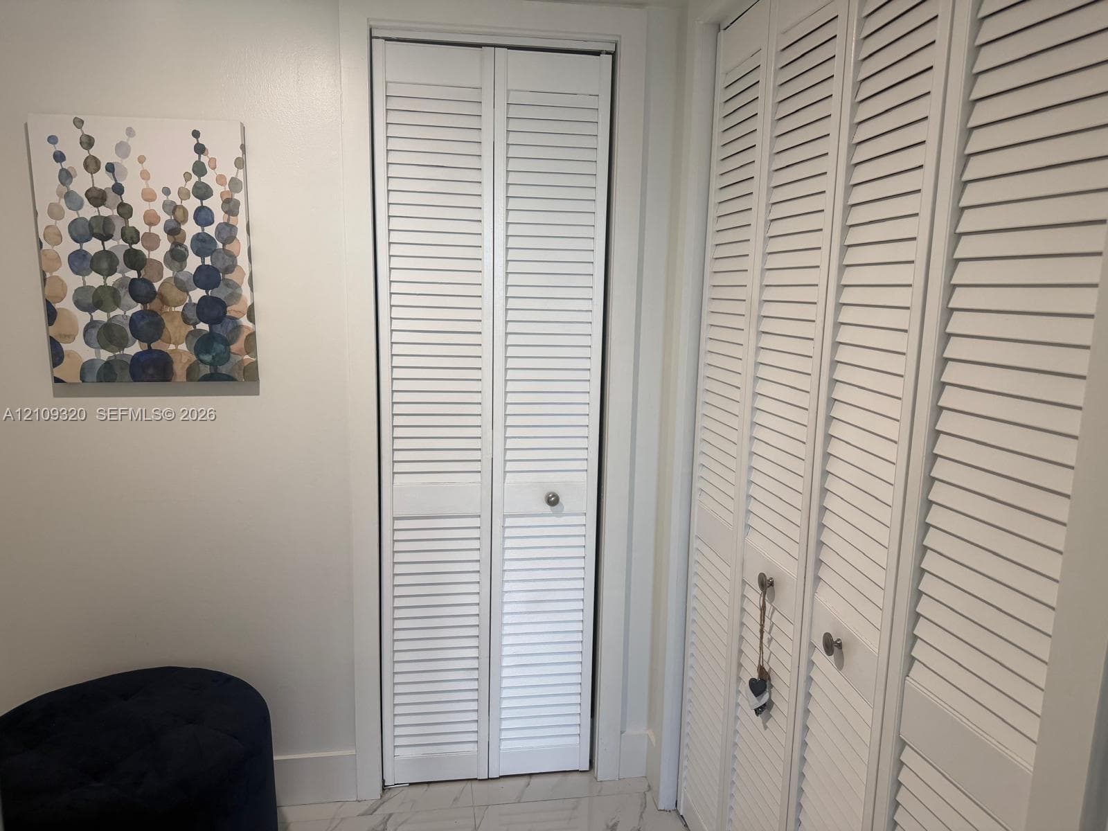 White bi-fold louvered closet doors with circular hardware, paired with stone-patterned flooring