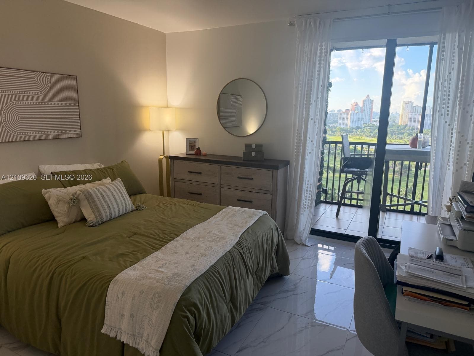 Floor-to-ceiling sliding glass doors opening to a balcony with metal railings, tile flooring, and urban skyline backdrop
