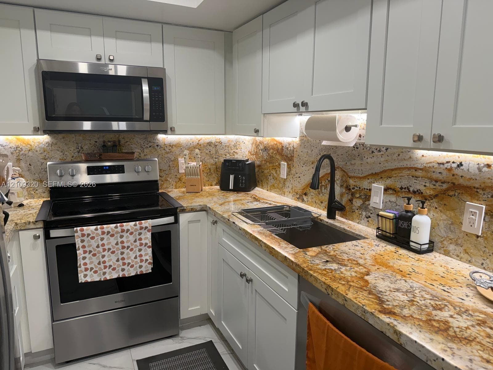Shaker-style cabinetry, patterned stone countertops, full-height stone backsplash, stainless steel appliances, and matte black arched faucet