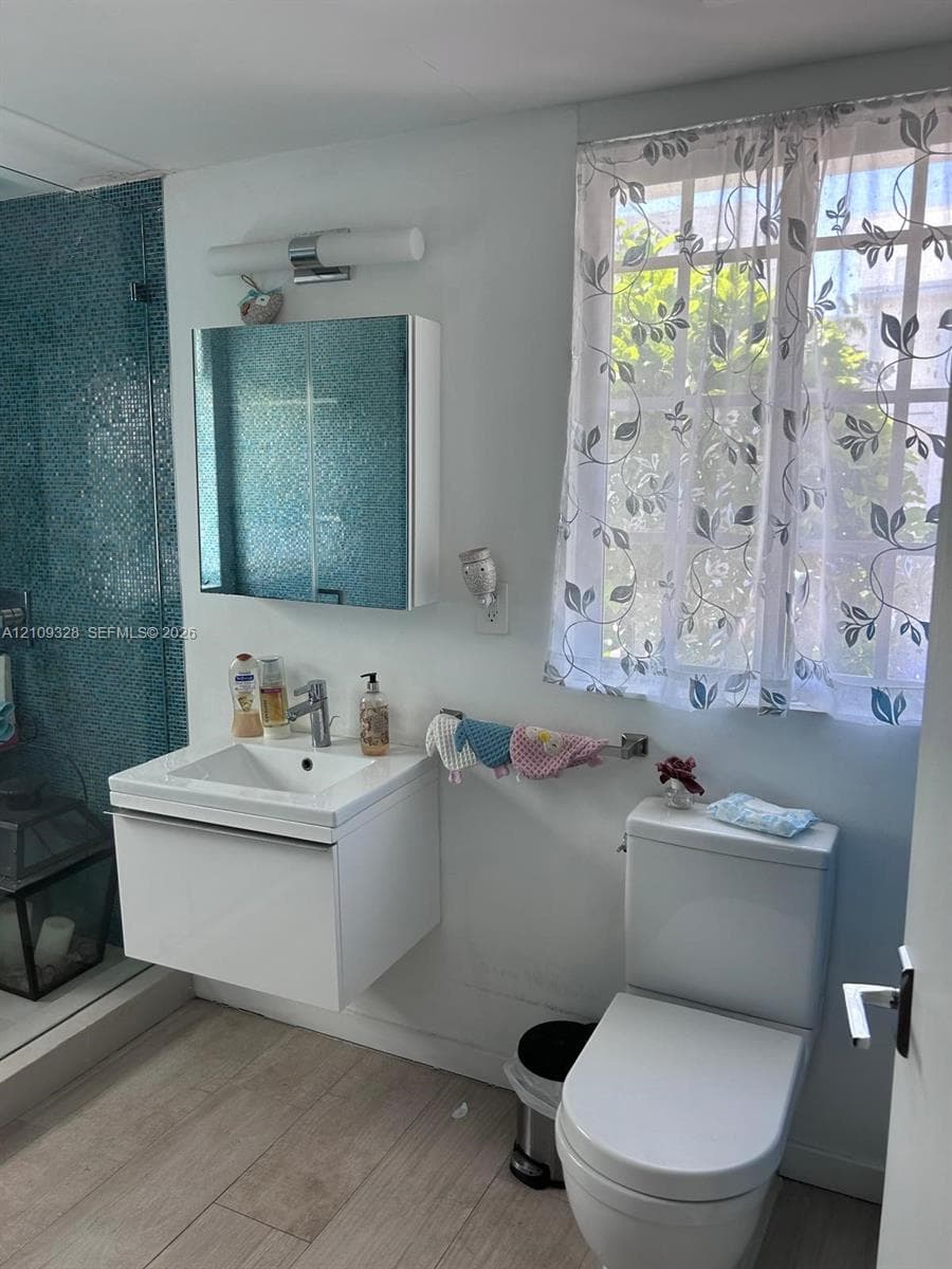 Floating white vanity with a single-basin sink, wall-mounted medicine cabinet, modern polished chrome faucet, and wood-finish flooring, complemented by a glass-enclosed shower featuring blue mosaic wall tiling
