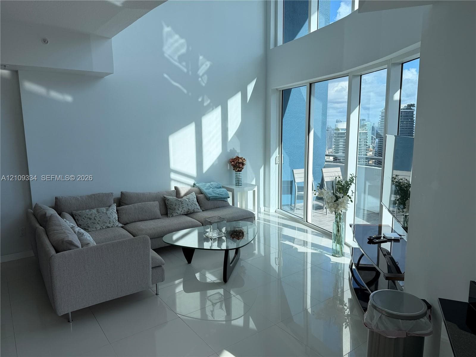 Double-height ceilings, floor-to-ceiling glass windows, polished tile flooring, and a private balcony