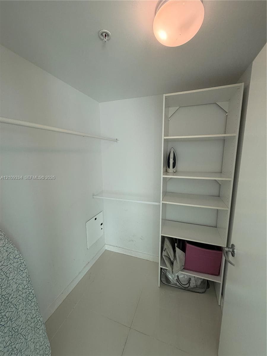 Walk-in storage space featuring built-in white shelving, a horizontal clothes rod, and tile flooring