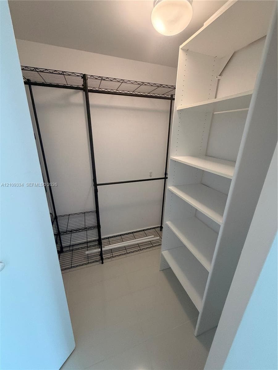 Walk-in closet featuring white laminate built-in shelving, black wire hanging racks, and a flush-mount ceiling light fixture