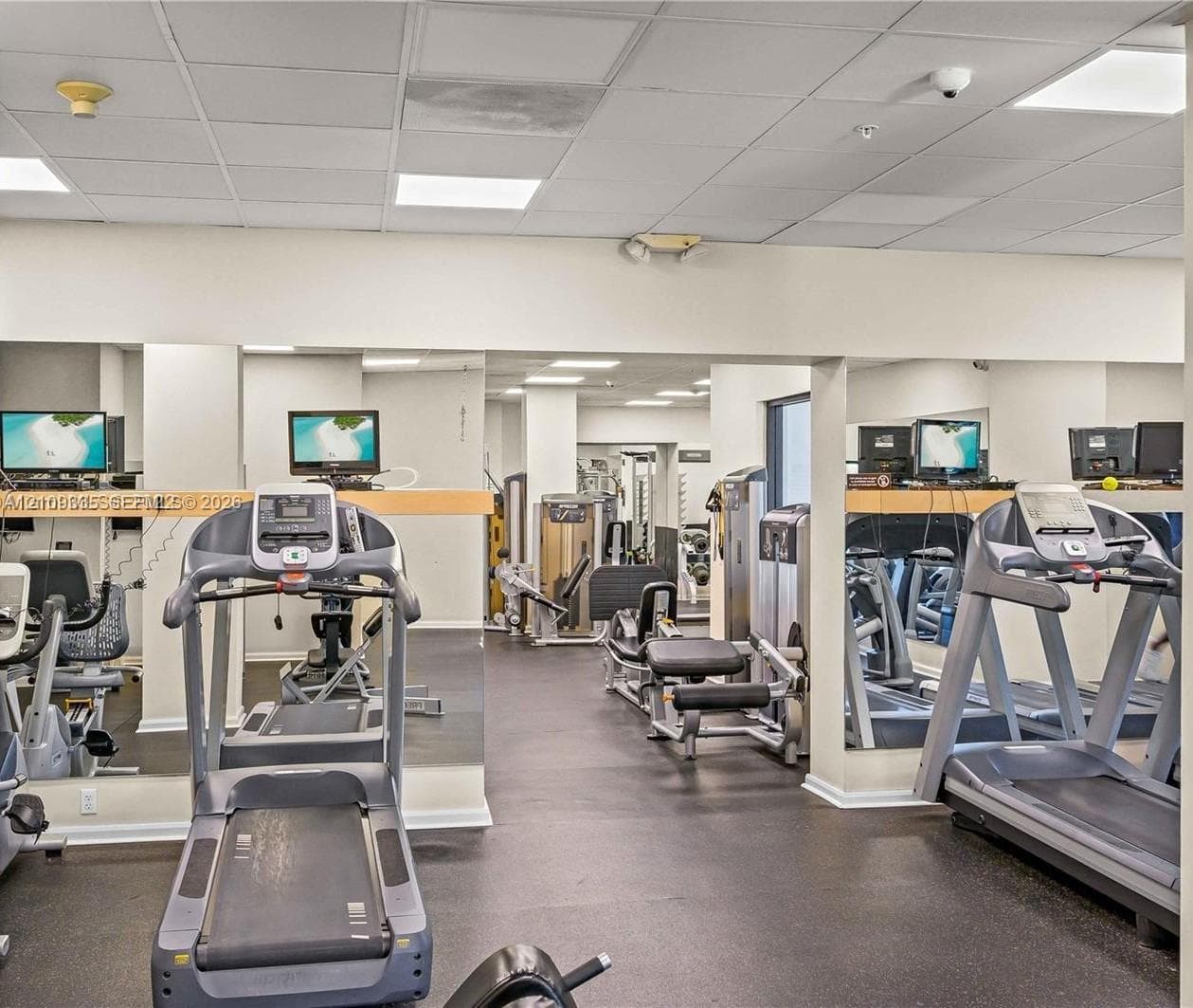 Fitness center featuring wall-to-wall mirrors, recessed drop-ceiling lighting, and specialized rubberized flooring