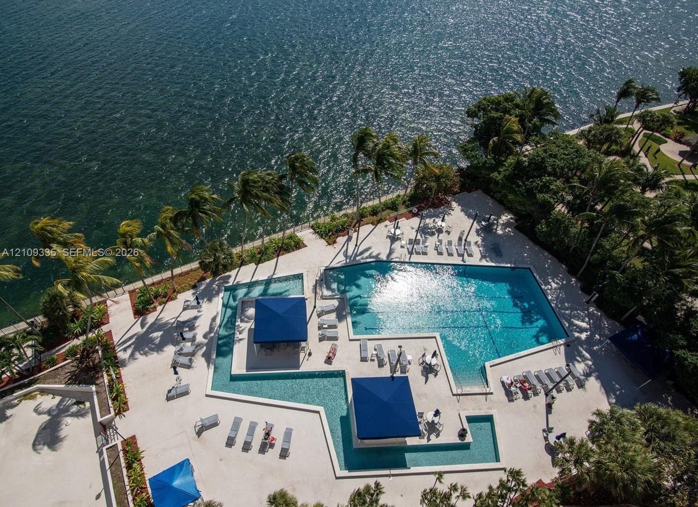 Waterfront swimming pool with sun shelf, multiple built-in shade structures, and concrete pool deck