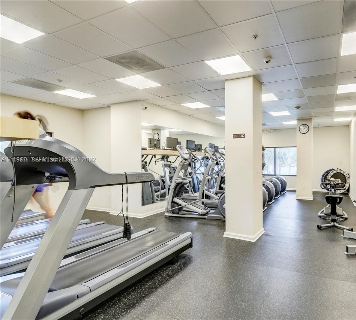 Fitness area featuring drop-ceiling tile grid, recessed lighting, wall-to-wall mirrors, and durable rubberized flooring
