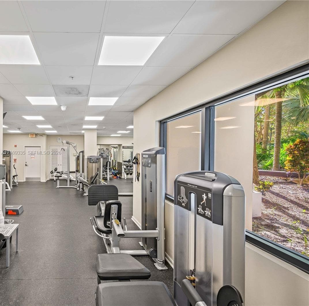 Fitness center featuring rubber flooring, recessed panel lighting, and large windows with outdoor vegetation