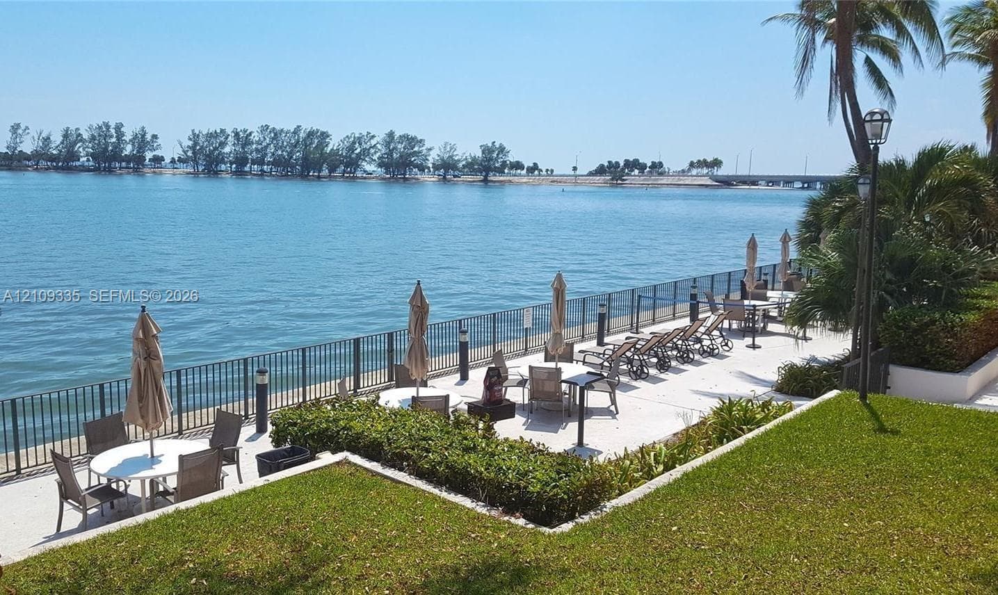 Waterfront terrace featuring a paved patio, perimeter metal fencing, mature landscaping, and integrated landscape lighting
