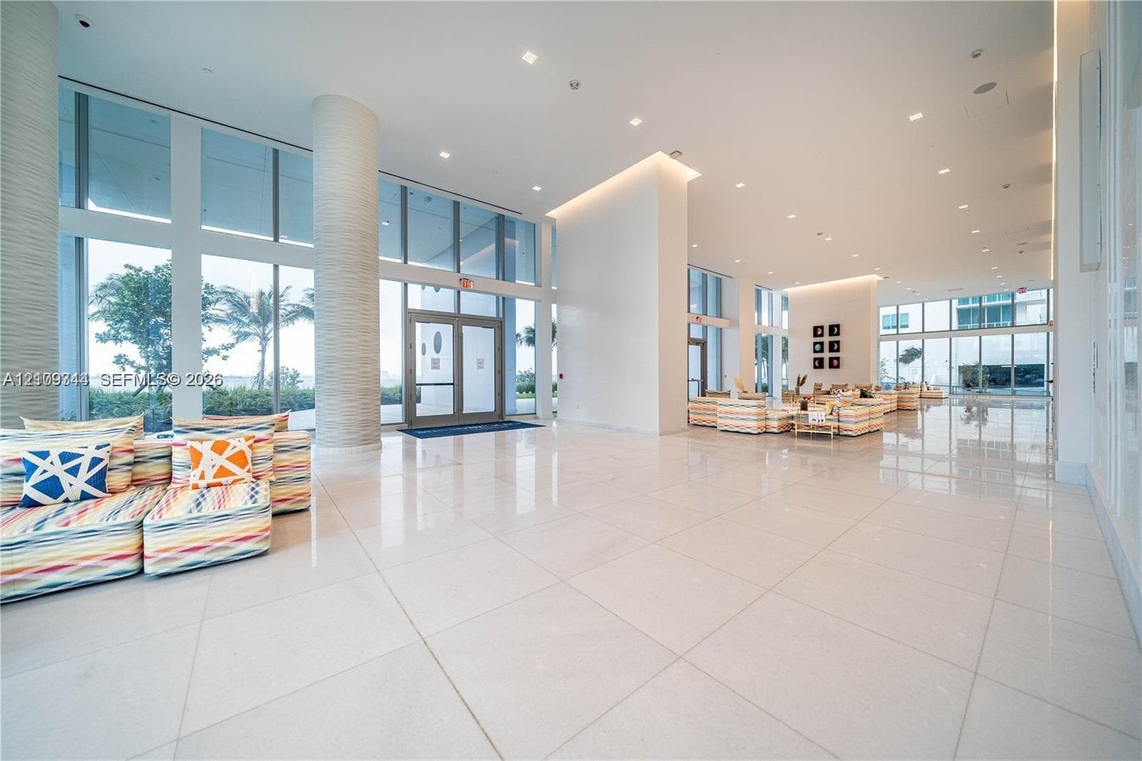 Expansive lobby featuring floor-to-ceiling glass walls, polished stone flooring, recessed ceiling lighting, and textured structural columns