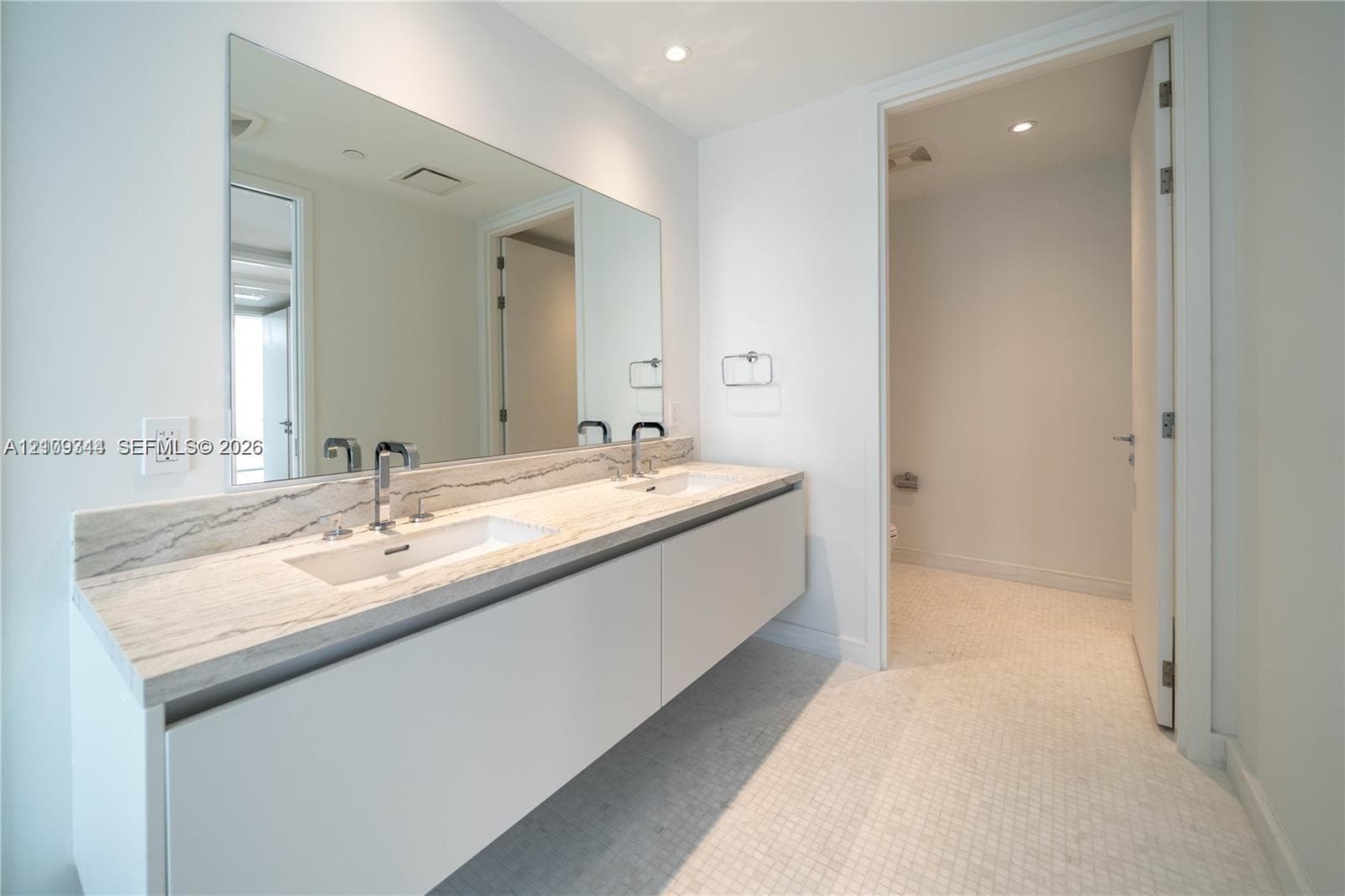Floating dual vanity with stone countertop, integrated sinks, chrome fixtures, full-width wall mirror, and mosaic tile flooring