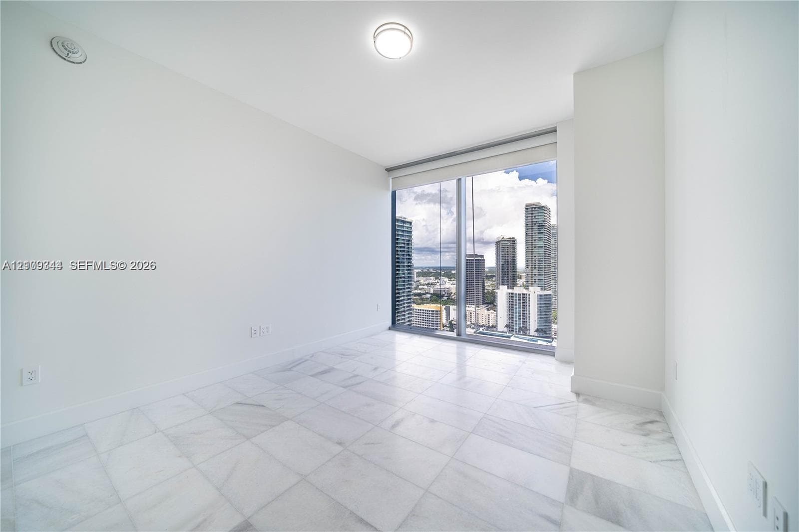 Floor-to-ceiling windows with urban skyline scenery, polished stone flooring, and a recessed ceiling lighting fixture
