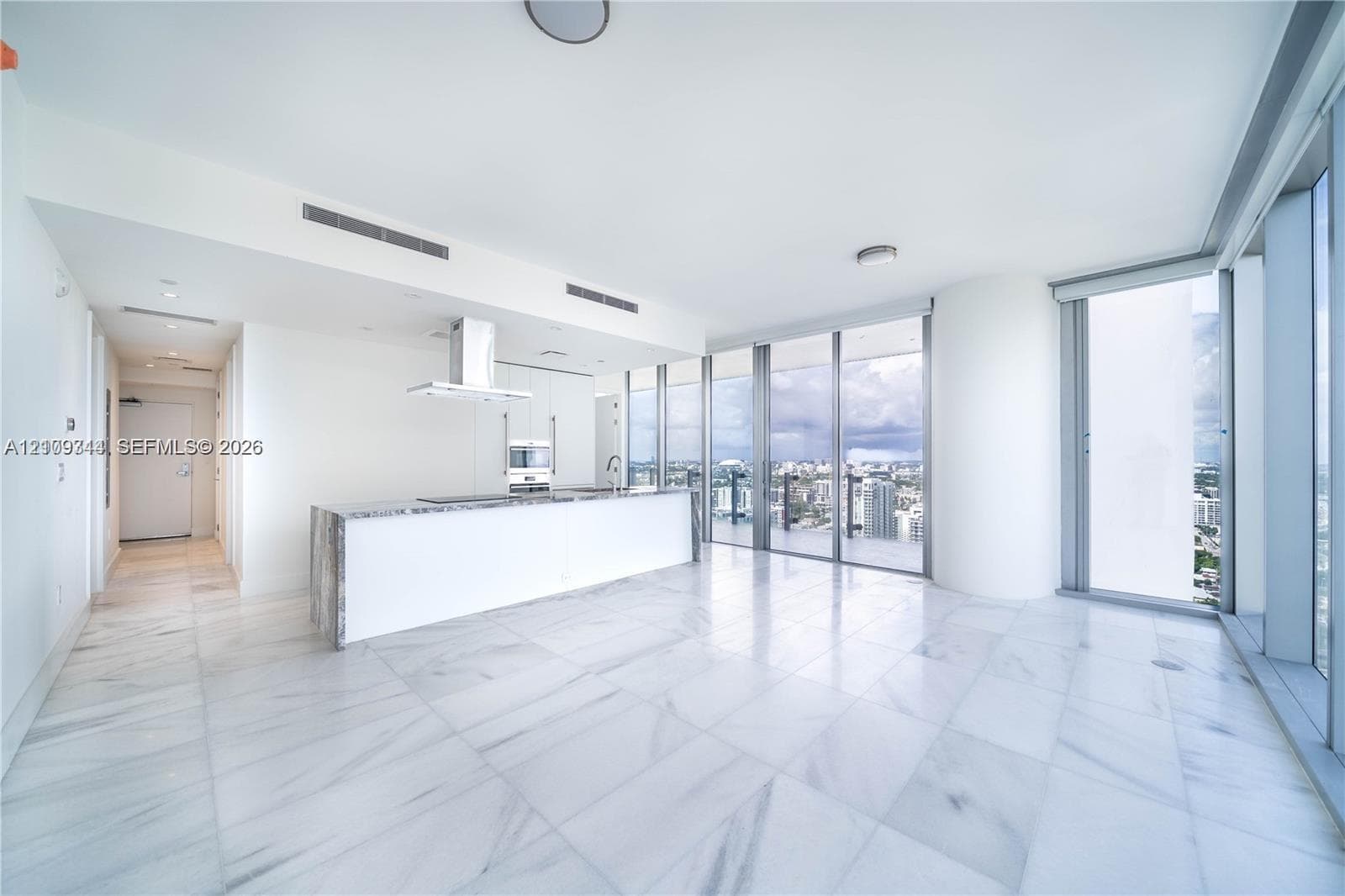 Open-concept interior featuring floor-to-ceiling glass walls, large-format stone-finish flooring, a kitchen island with stone-finish waterfall edges, and a stainless steel range hood