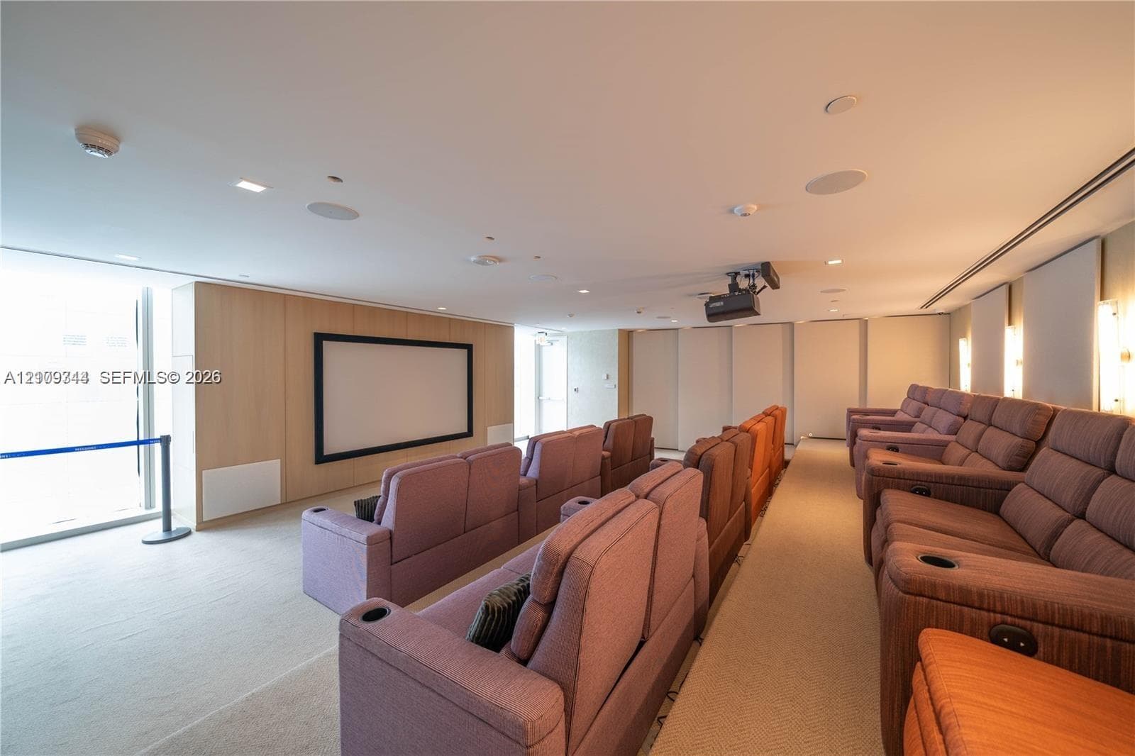 Media room featuring tiered seating, recessed ceiling lighting, wall-mounted projector, and light-toned wood-finish paneling