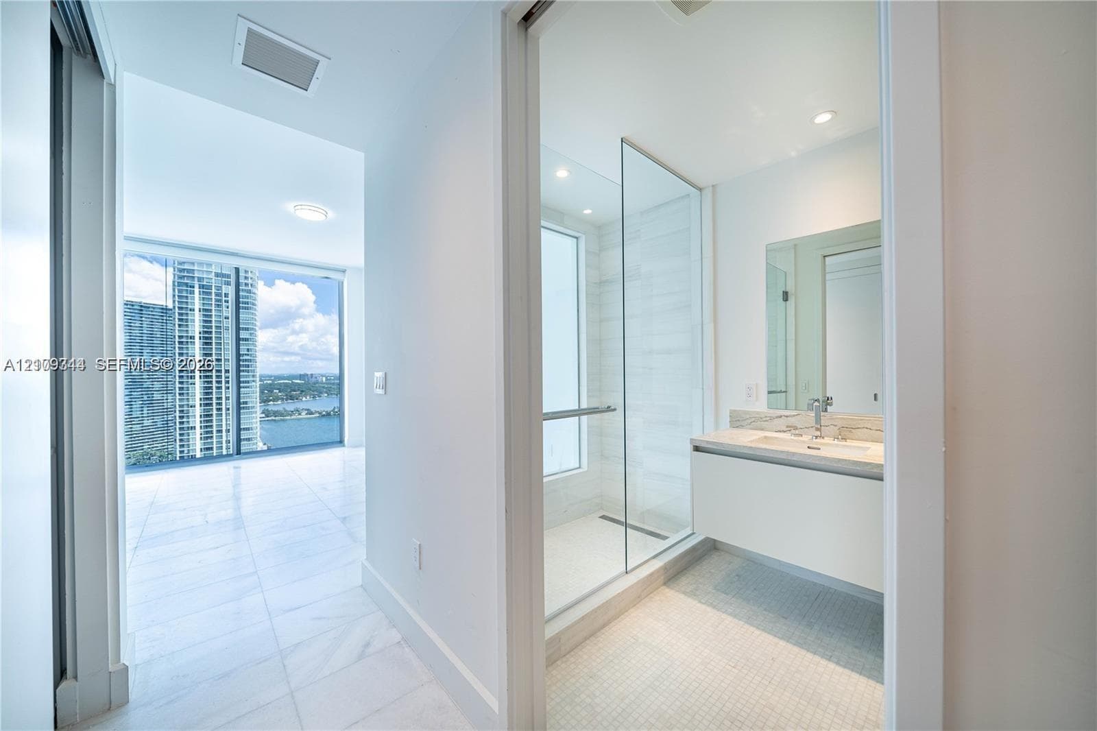 Bathroom featuring a floating vanity with stone countertop, frameless glass-enclosed shower, wall-mounted faucet, and floor-to-ceiling windows with water scenery