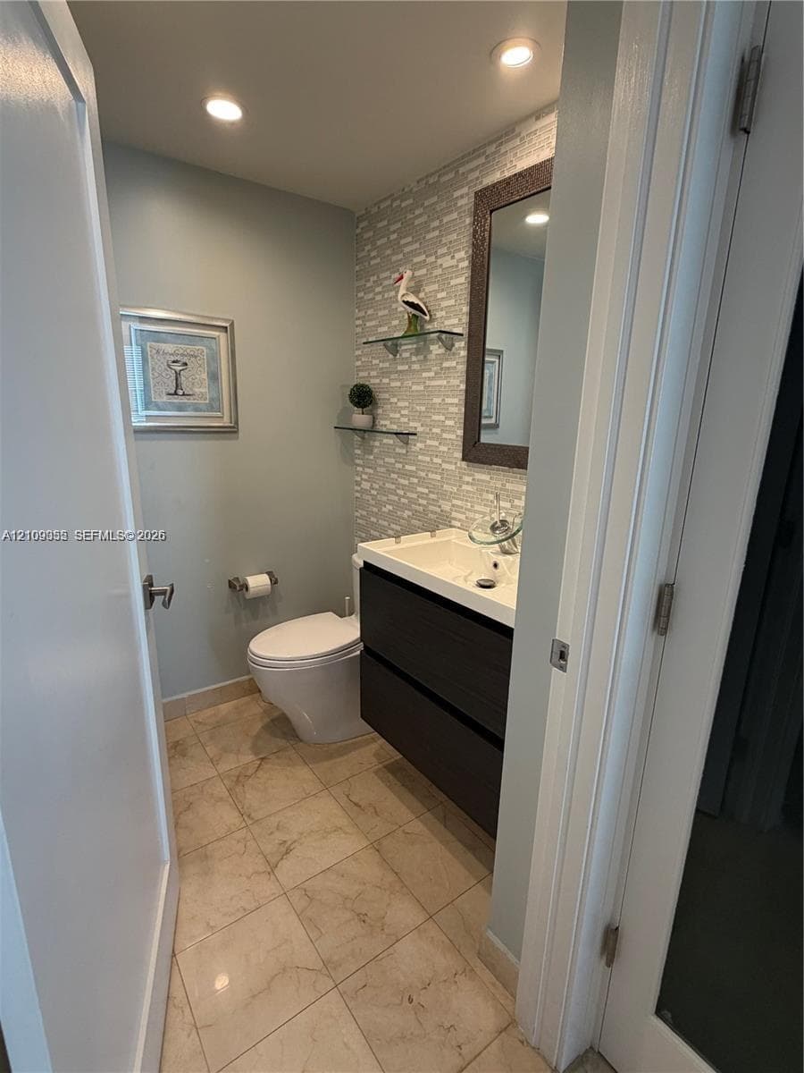 Modern powder room featuring a wall-mounted floating vanity, textured tile accent wall, recessed ceiling lighting, and tile flooring