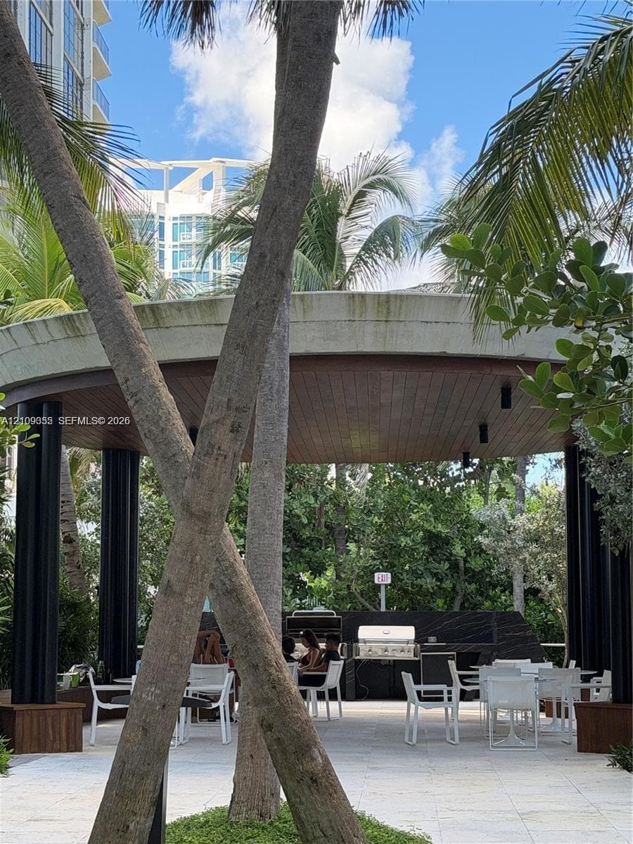 Outdoor pavilion featuring a circular concrete roof, wood-plank ceiling, black support columns, built-in stone-finish grill station, and stone-tile patio flooring