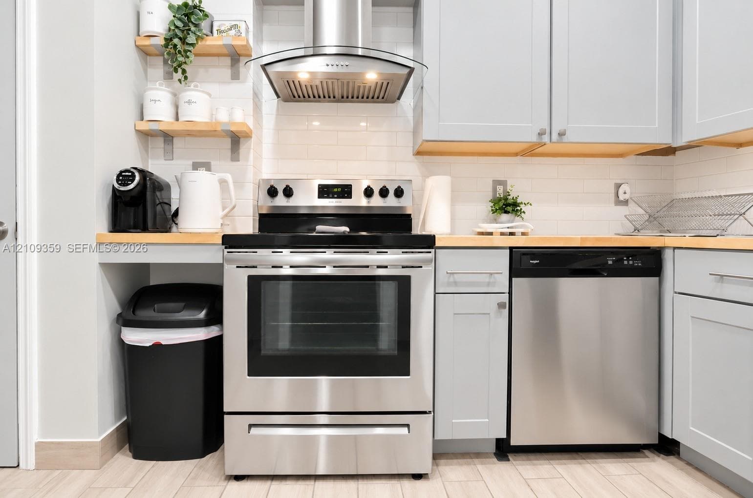 Kitchen featuring light-toned cabinetry, wood countertops, stainless steel appliances, a subway tile backsplash, and wall-mounted shelving