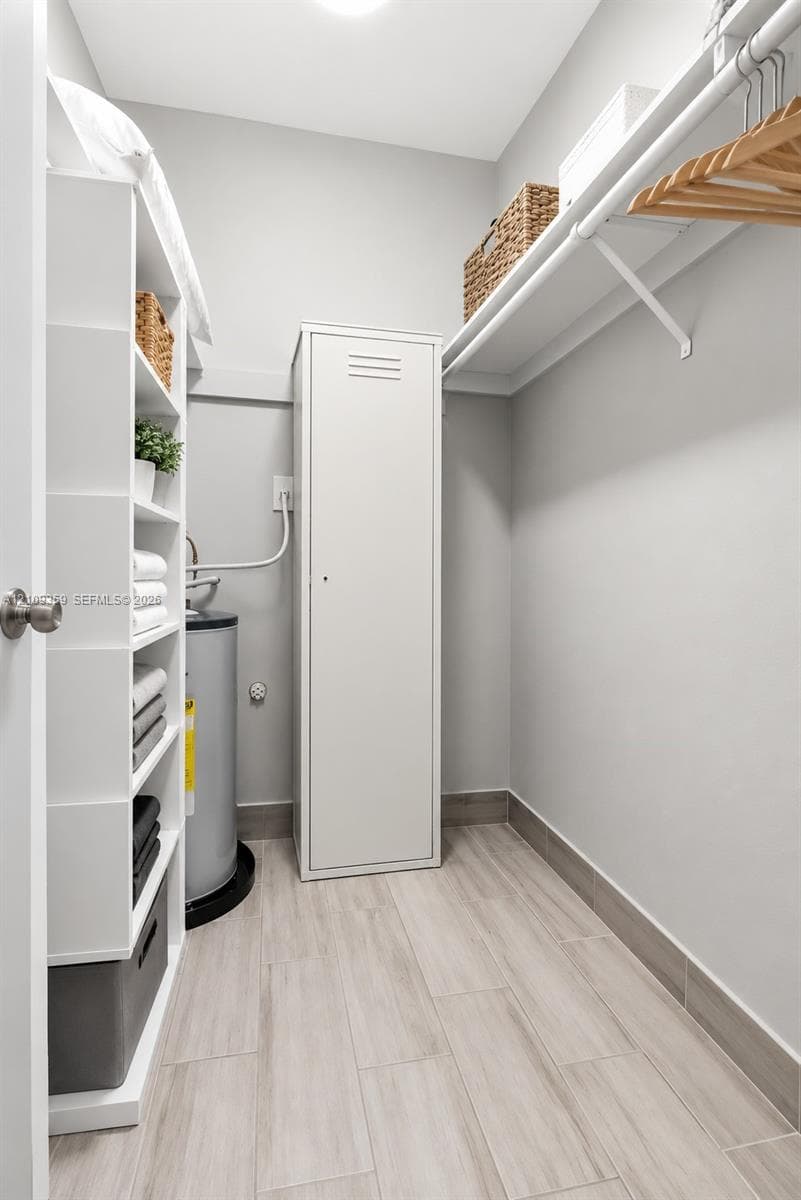 Storage space featuring built-in white shelving, a full-height metal cabinet, wall-mounted hanging rod, and wood-finish tile flooring