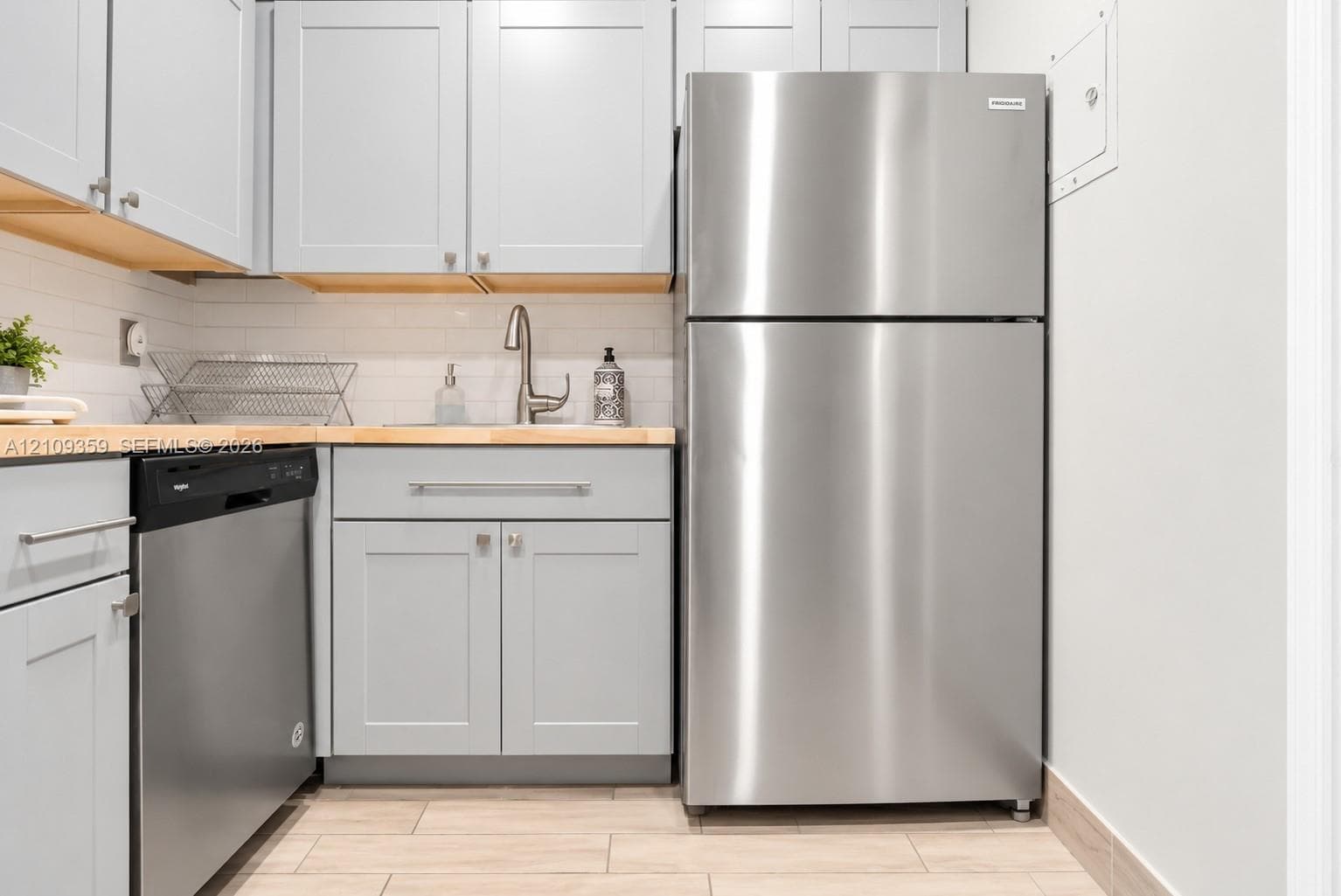 Kitchen featuring shaker-style grey cabinetry, wood-tone countertops, stainless steel appliances, a white subway tile backsplash, and ceramic tile flooring