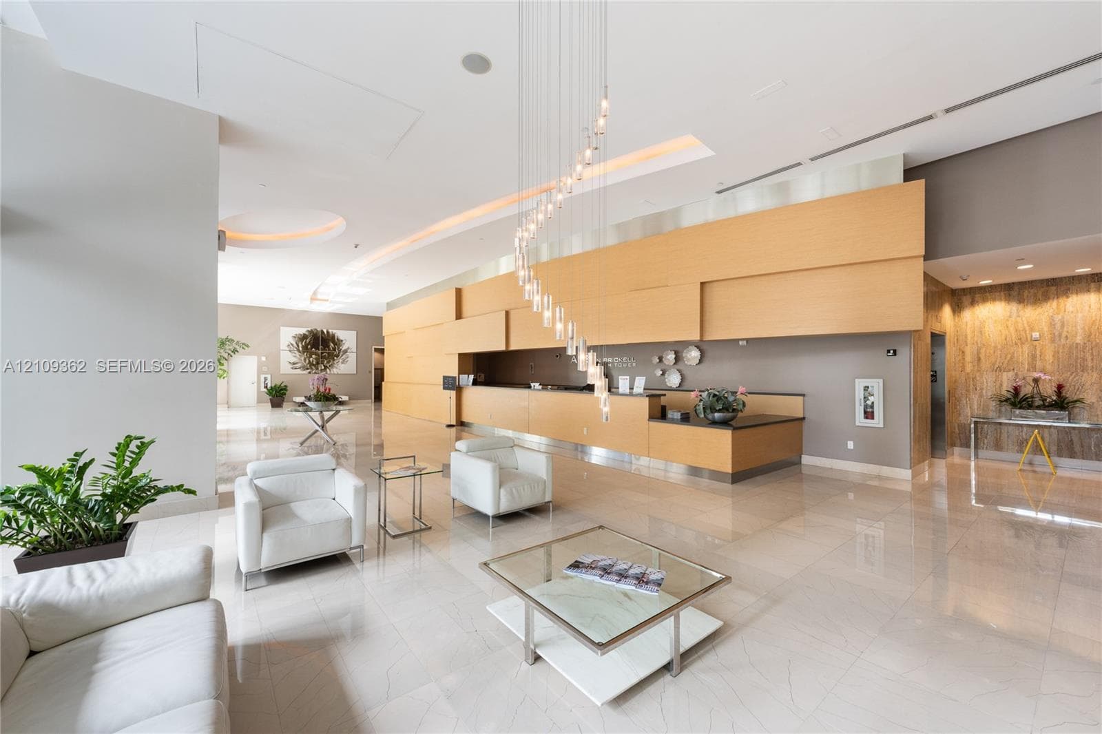 Spacious lobby featuring polished stone flooring, a multi-tiered spiral crystal chandelier, built-in reception desk with wood paneling, recessed lighting, and a textured stone feature wall