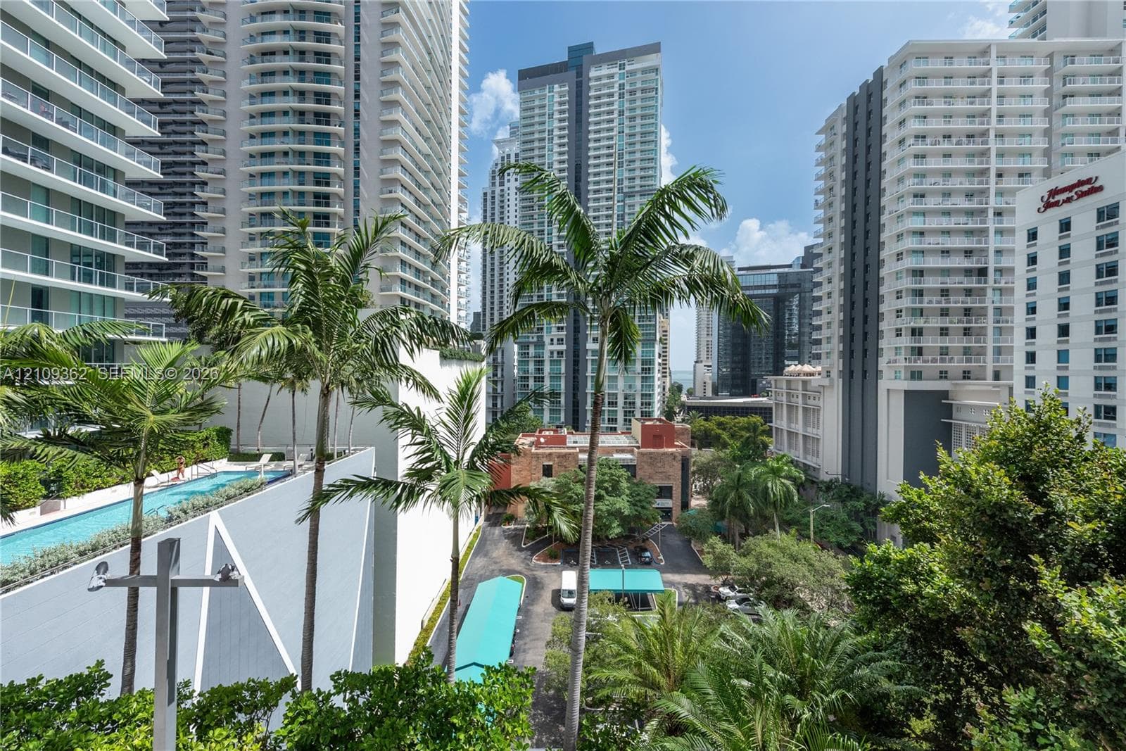 Elevated urban perspective featuring high-rise architecture, a rooftop lap pool, palm trees, and paved grounds