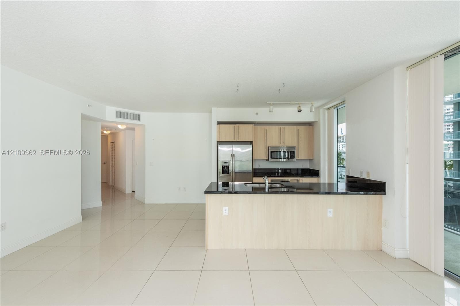 Kitchen featuring light-finish cabinetry, dark stone countertops, stainless steel appliances, a peninsula with an integrated sink, and large-format tile flooring