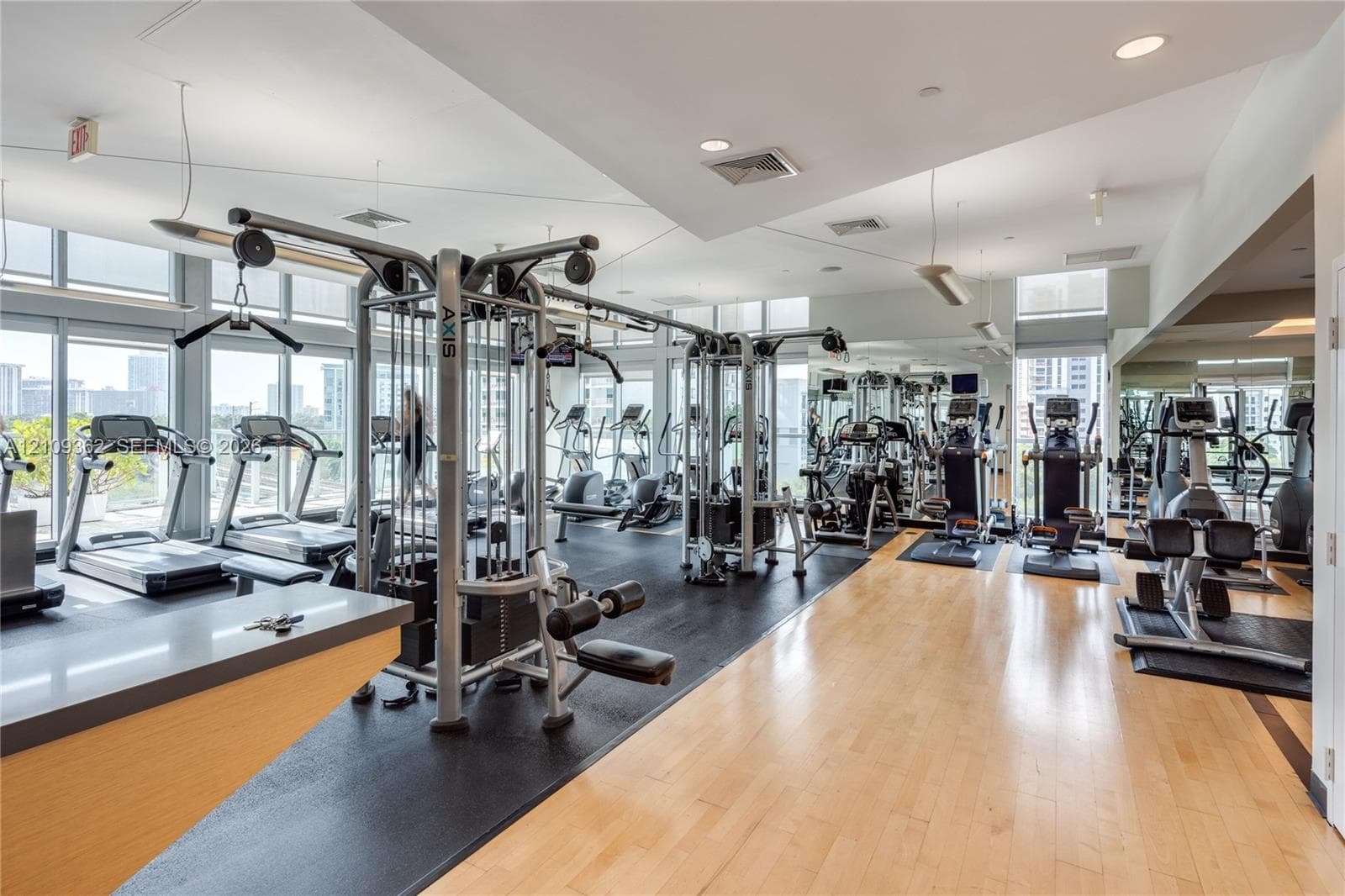 Fitness center featuring floor-to-ceiling windows, light-toned wood-finish flooring, rubberized workout surfacing, recessed lighting, and mirrored walls