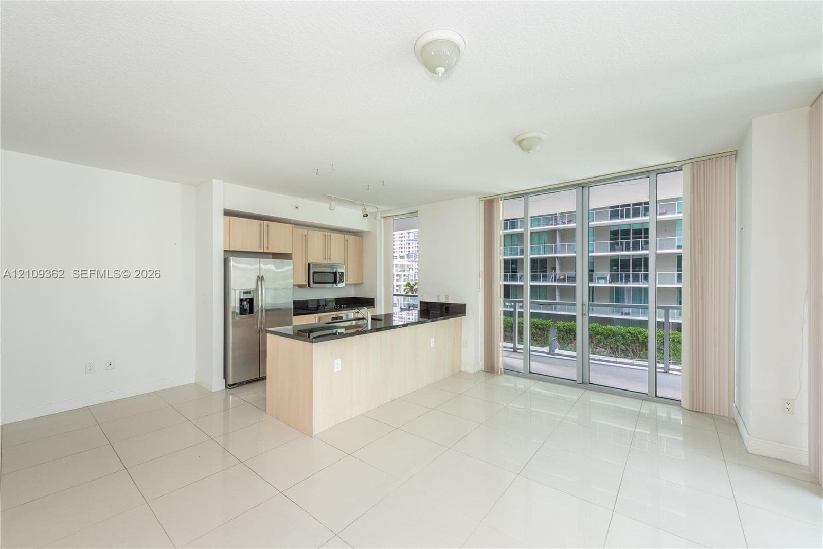 Kitchen featuring light-finish cabinetry, dark stone countertops, stainless steel appliances, tile flooring, and floor-to-ceiling glass sliding doors