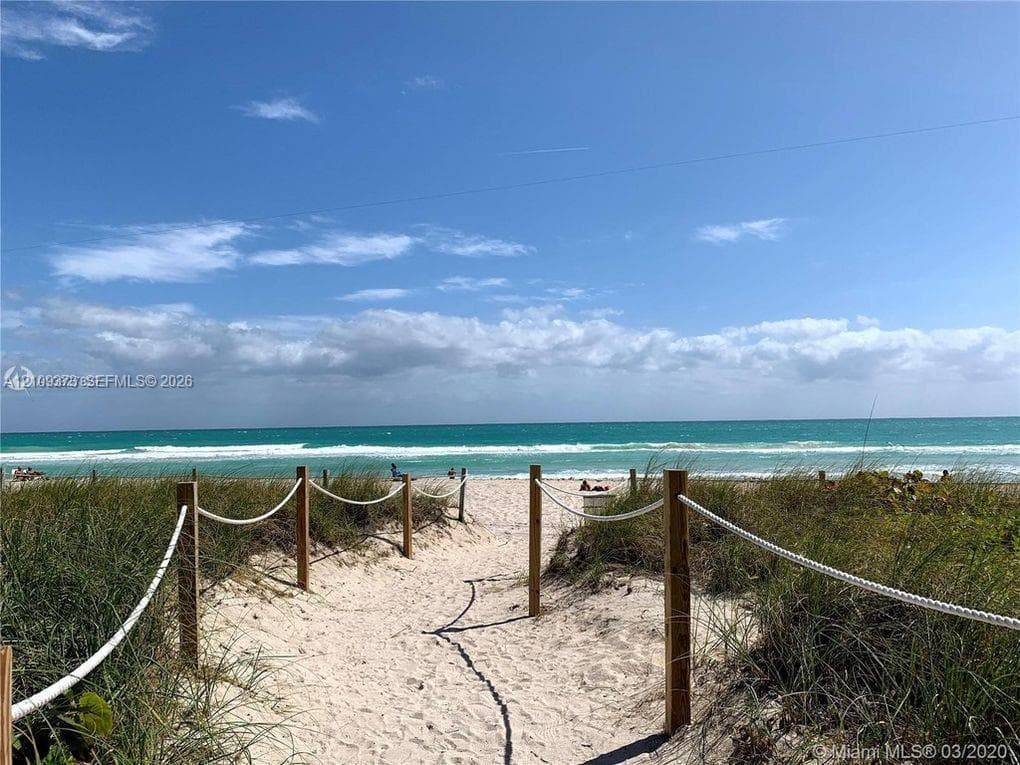 Sandy beach access featuring a sand pathway, wood post-and-rope perimeter, and coastal dune vegetation